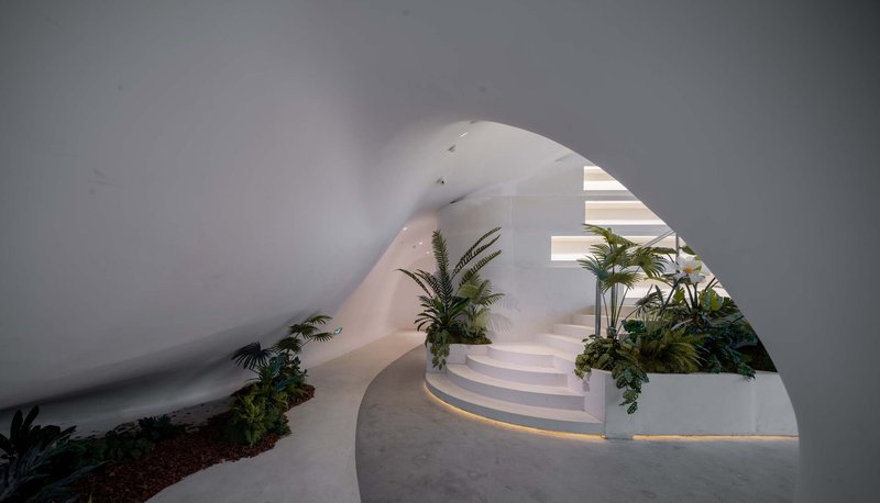 Curved white staircase framed by an arched opening with planted beds along the edges