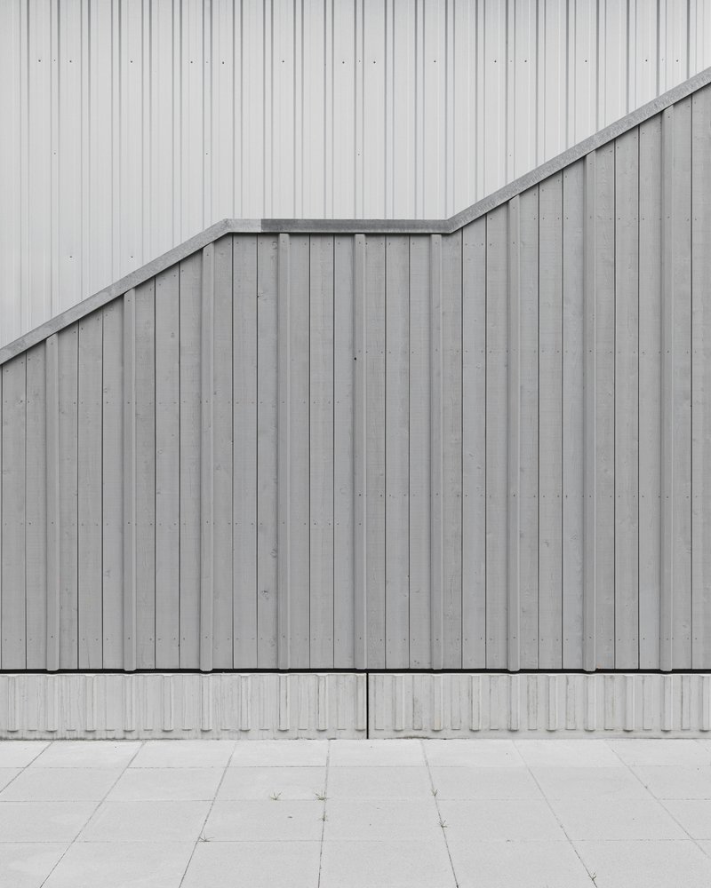 Exterior detail of vertical metal panel facade with angular roofline meeting concrete pavers