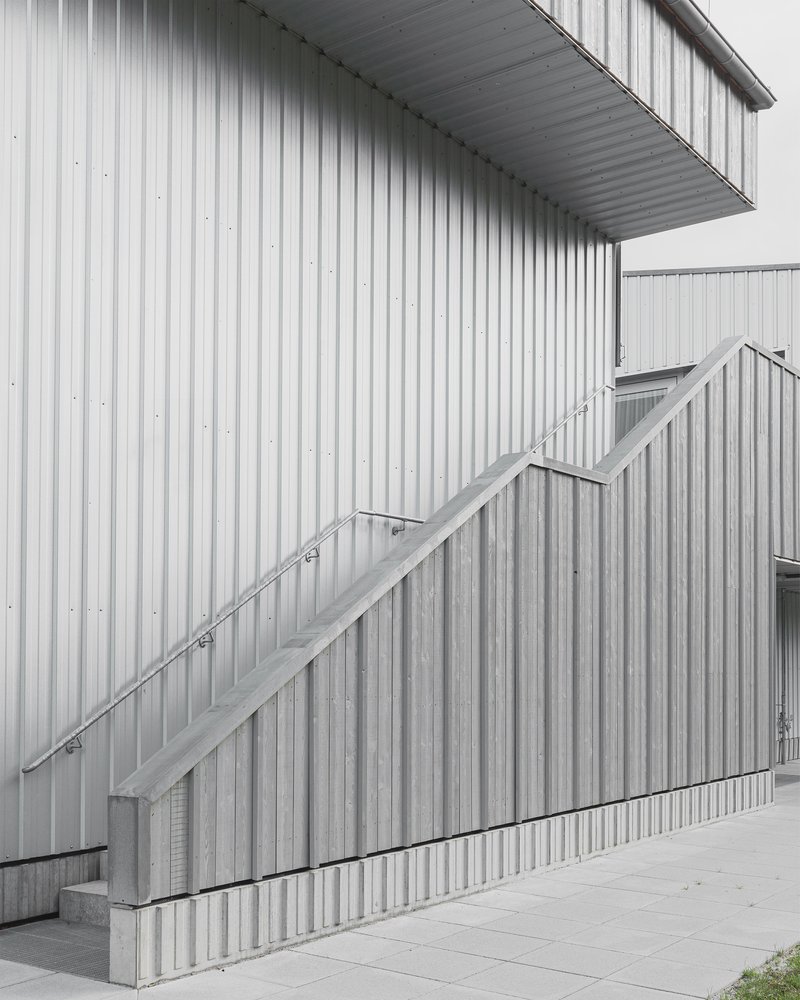 Exterior staircase with metal handrail ascending corrugated metal panel cladding on an overcast day