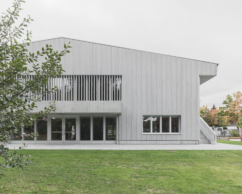 Facade with vertical batten screen balcony above glazed ground floor openings framed by trees