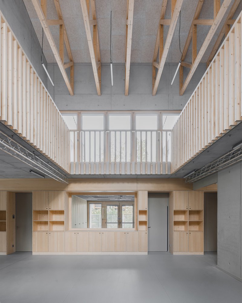 Double-height hall with exposed timber rafters, vertical batten screens and plywood storage units below