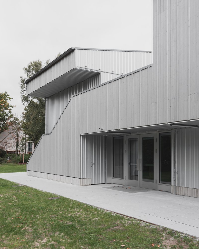 Angled canopy projection above glass doors and concrete terrace on corrugated metal volume