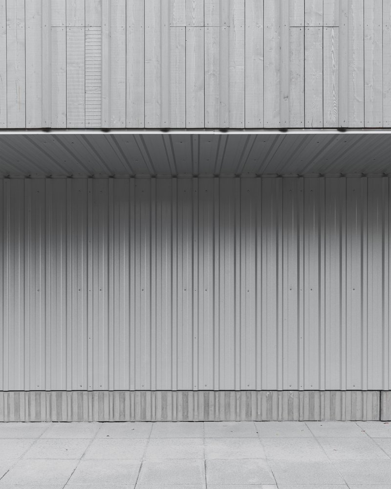Covered entry with vertical metal cladding and weathered timber facade above a concrete paver courtyard