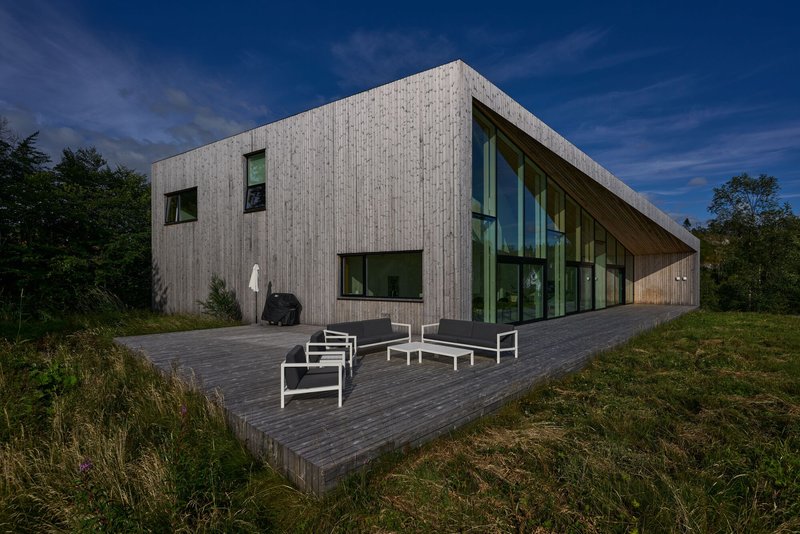Vertical wood-clad facade with scattered windows and a cantilevered timber deck at dusk