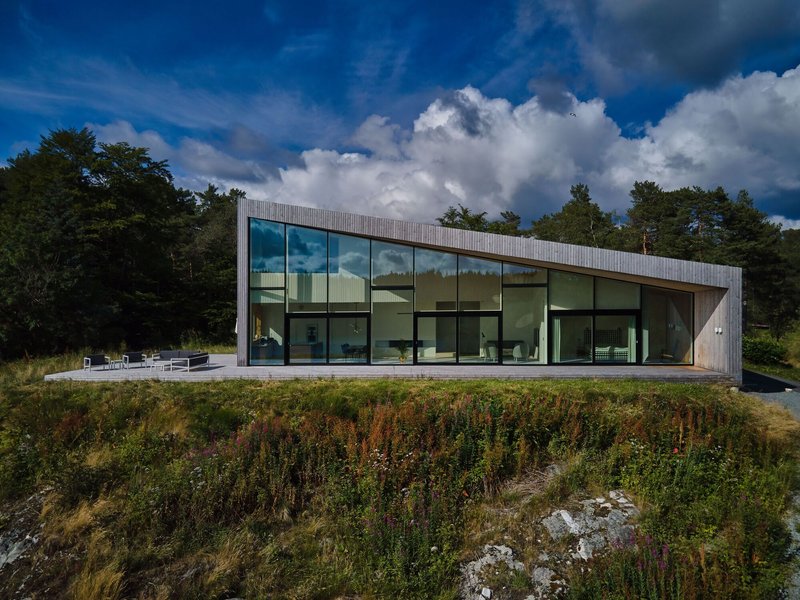 Glass wall facade reflecting clouds with native grasses and wildflowers in the foreground