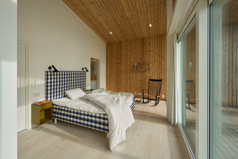 Bedroom with timber accent wall and pale wood flooring opening to a glass-walled terrace