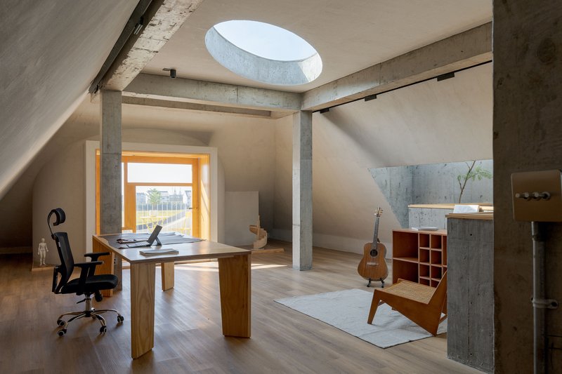 Home office with timber desk and acoustic guitar beneath circular skylight and exposed concrete columns