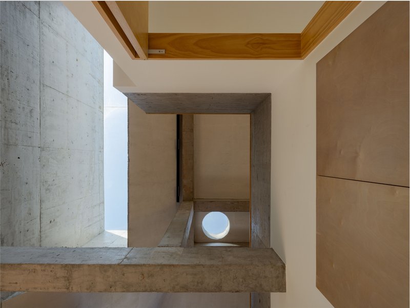 View down through a concrete frame opening showing timber stairs and a circular window below