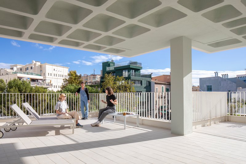 Rooftop terrace with coffered concrete ceiling and white vertical railing under midday sun