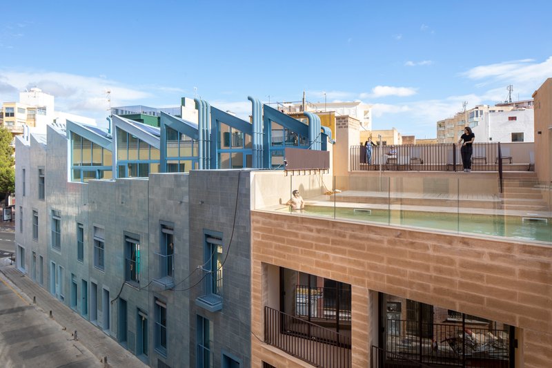 Rooftop terrace with glass railings and swimming pool overlooking sawtooth glazed volumes under afternoon light