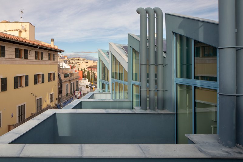 Rooftop terrace showing three industrial ducts and angled glass pavilions against a cloudy sky