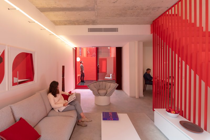 Interior with red slatted staircase screen and view through glazed courtyard where two people stand