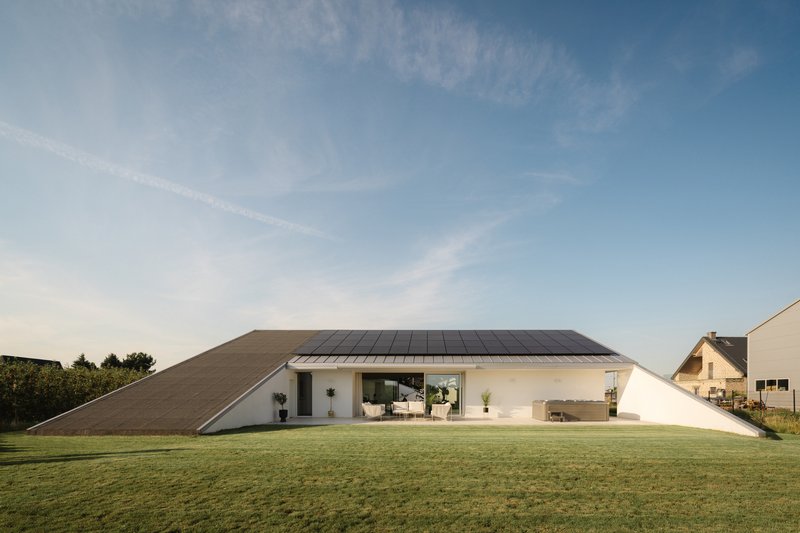 Sloped roof with solar panels rising from a white rendered facade across a manicured lawn at dusk