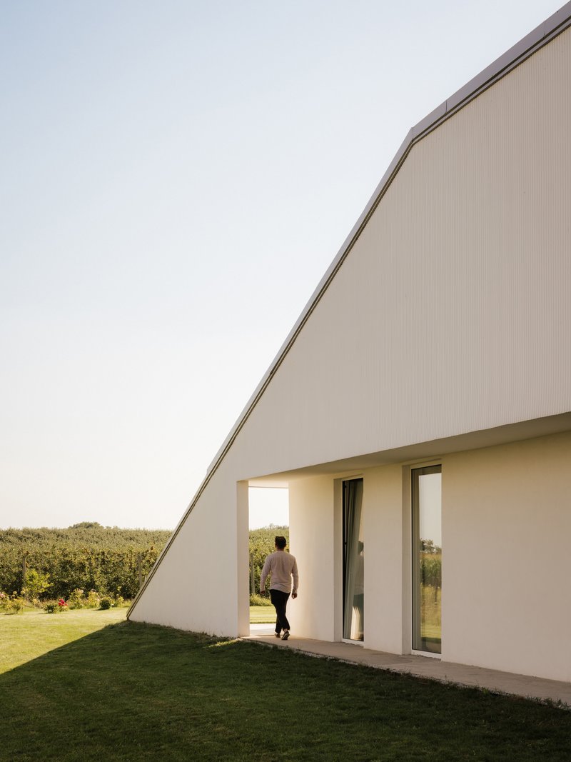 Diagonal roofline meeting white rendered walls as a person walks through the covered exterior passage