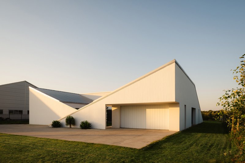 Illuminated garage door beneath folded roofline with metal cladding at golden hour