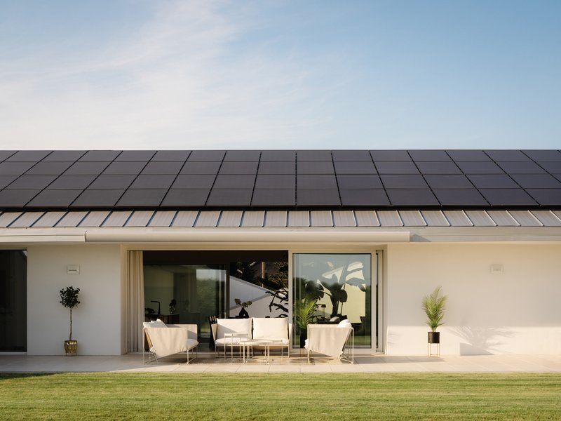 Exterior terrace with sliding glass doors beneath a dark standing-seam metal roof and open lawn