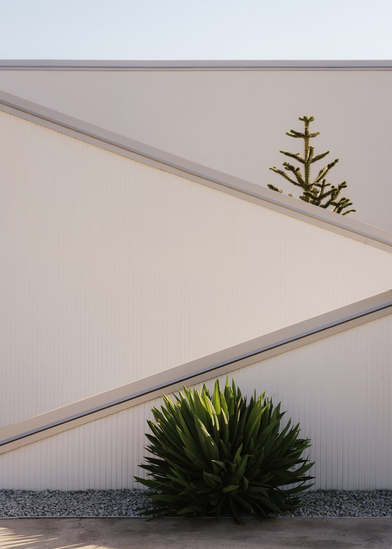 Layered white stucco parapets with vertical ribbed panels and plantings in gravel bed at dusk