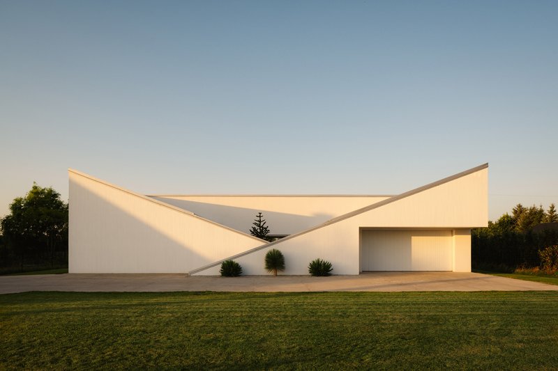 Front facade with twin angled roof volumes and recessed garage opening at sunset
