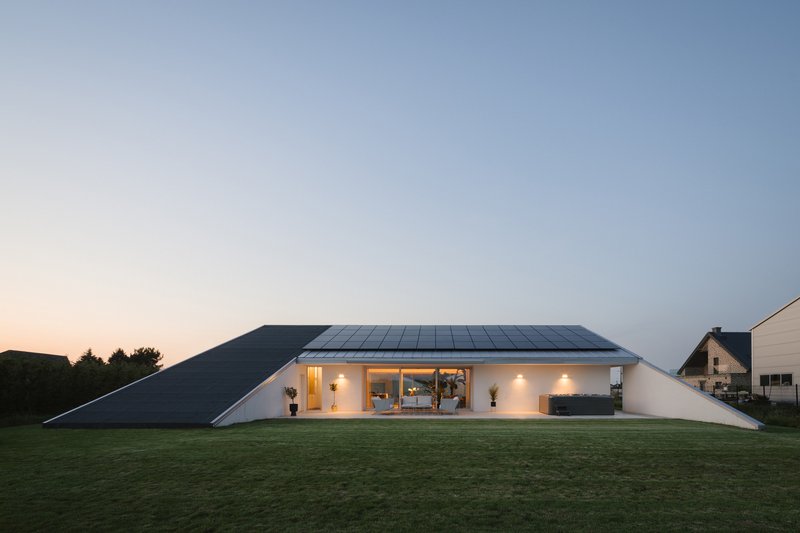 Frontal view of the solar panel roof and glazed living space at dusk with lawn in foreground