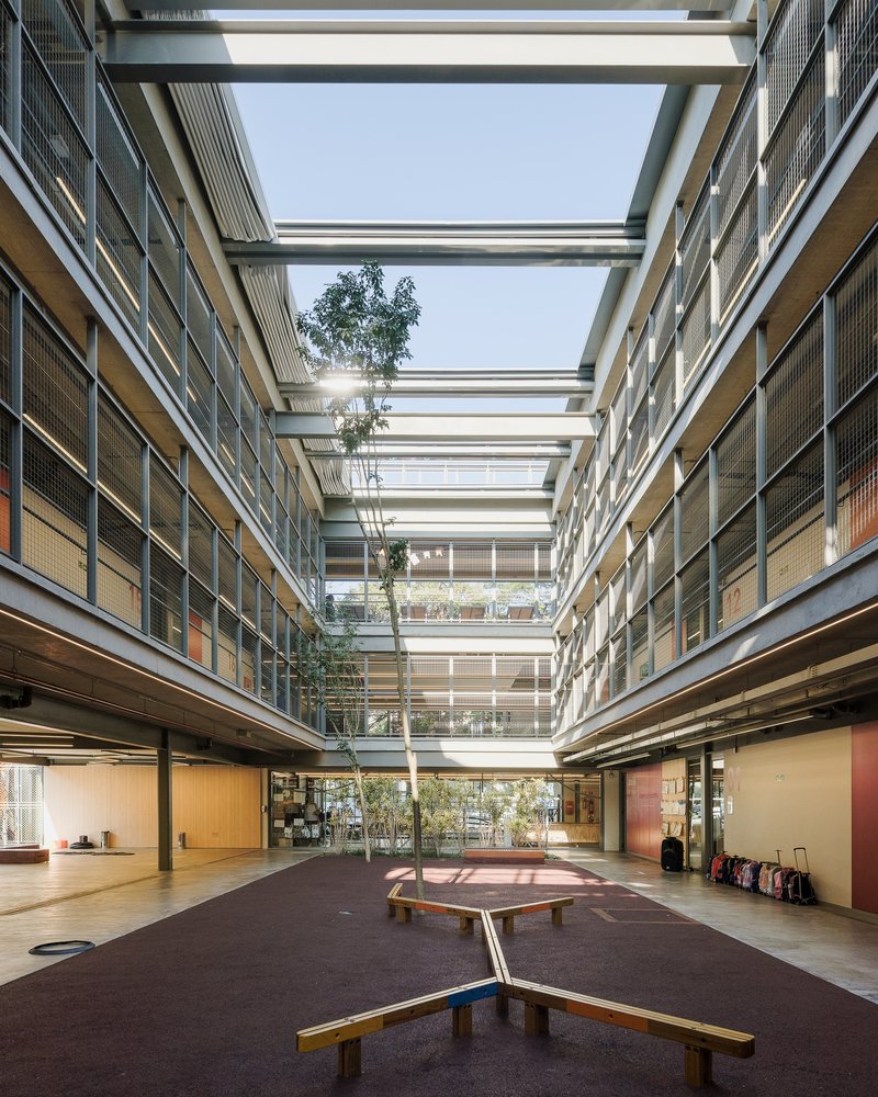 Central courtyard with timber benches and planted trees beneath horizontal roof beams spanning four levels