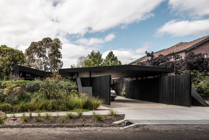 Street view of the cantilevered carport with vertical timber cladding and native grasses along the driveway
