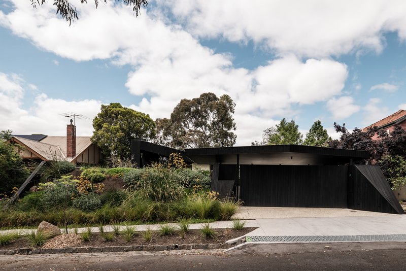 Street view of the black timber and concrete facade behind native grasses and gravel beds
