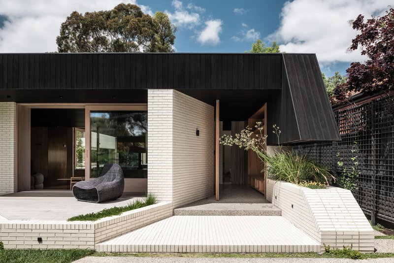 Courtyard view with cream brick walls, timber threshold, and angled black cladding against the planted boundary