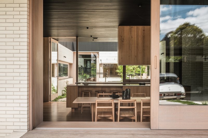 View through sliding doors to the dining area with timber table and chairs beneath a dark slatted ceiling