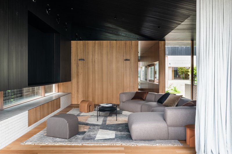 Living room with sectional sofa and timber storage wall beneath a dark timber slatted ceiling
