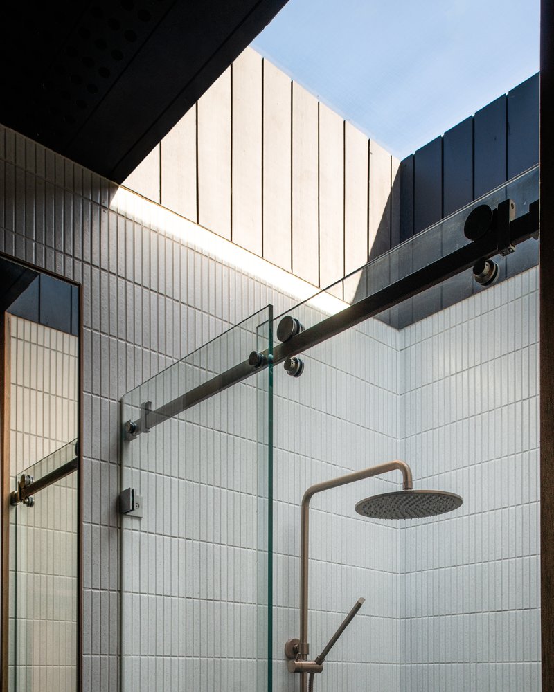 Open-air shower enclosure with glass partition and skylight above white vertical tile walls