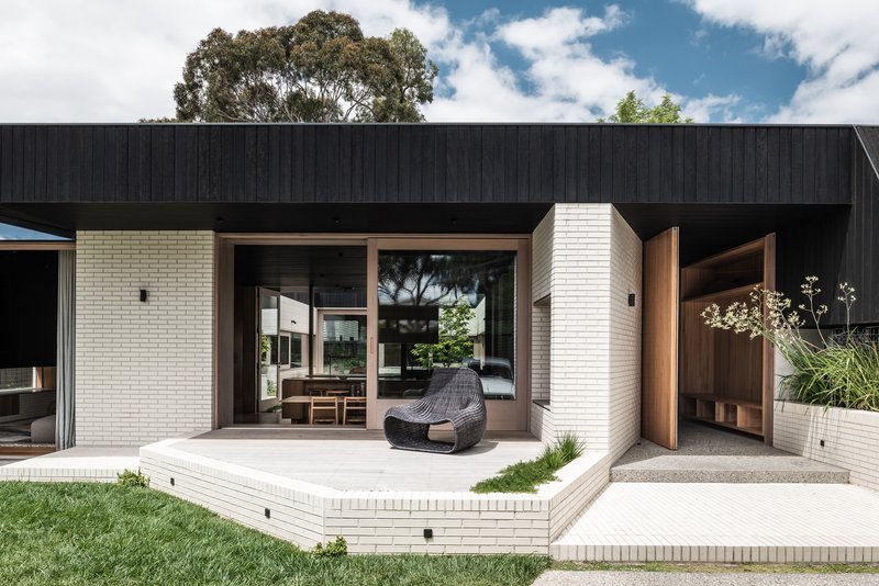 Raised concrete terrace with woven lounge chair facing glazed openings and cream brick planters