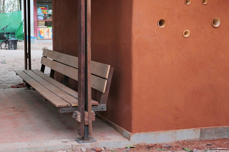 Timber bench against a red ochre wall with circular apertures and steel column