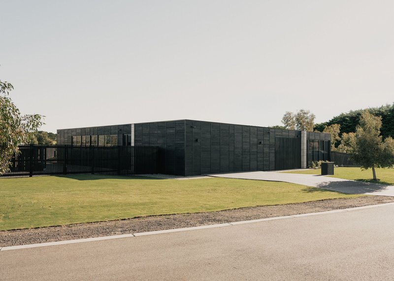 Corner view showing the charred timber cladding and vertical slat fence with trees in the background