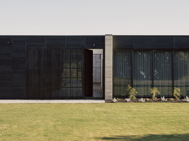 Close-up of the entry with vertical timber screen and concrete column against the dark cladding