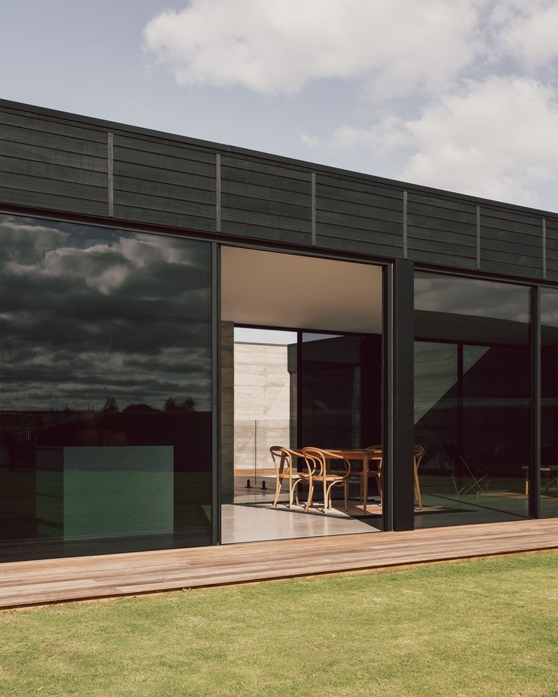 Timber deck and open sliding doors framing the dining table beneath darkening storm clouds