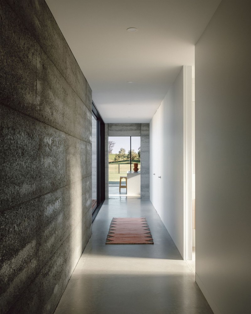Concrete hallway with polished floor and cove lighting leading toward pool terrace in daylight