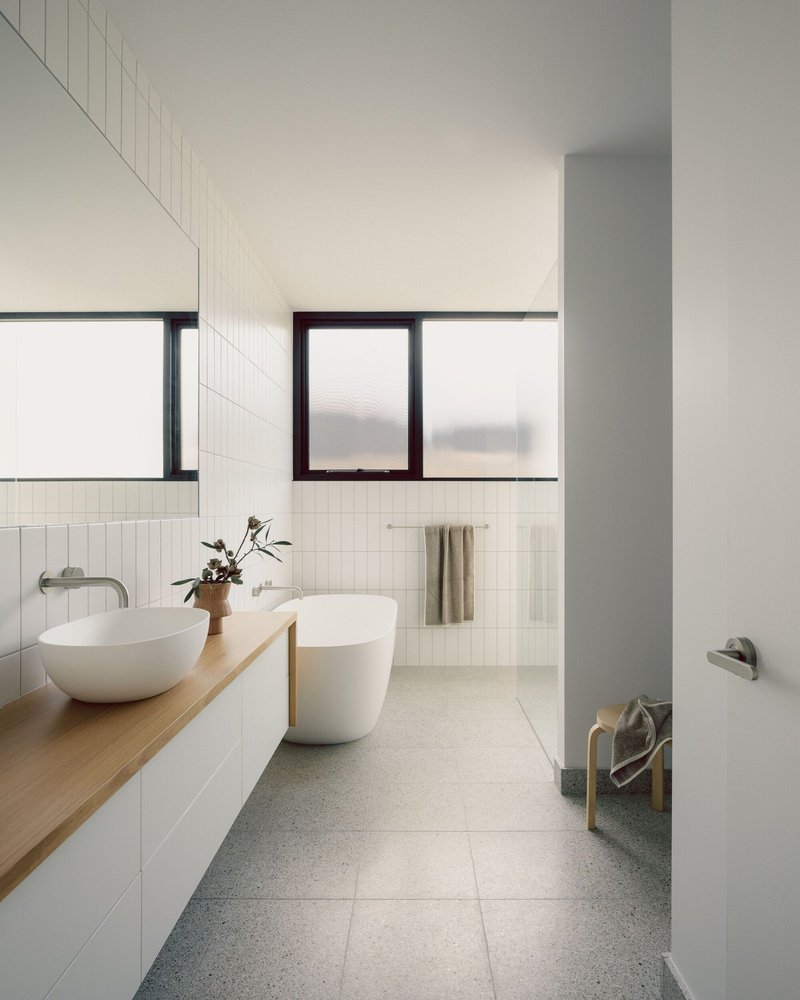 Bathroom with white vertical tile walls, timber vanity and freestanding tub beside terrazzo flooring