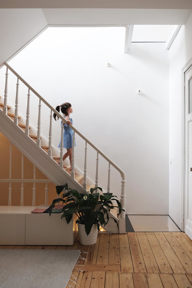 White painted timber staircase with turned balusters and a child descending under bright skylights
