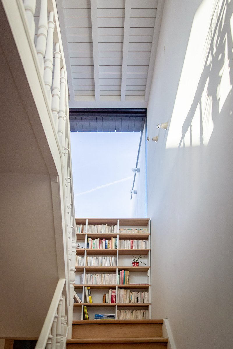 View up the stairwell showing timber bookshelves at the landing under a skylight and white-painted ceiling