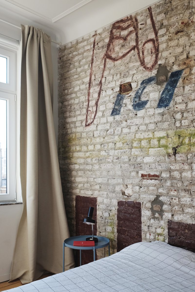 Exposed whitewashed brick wall with faded painted signage in a bedroom corner with draped curtains