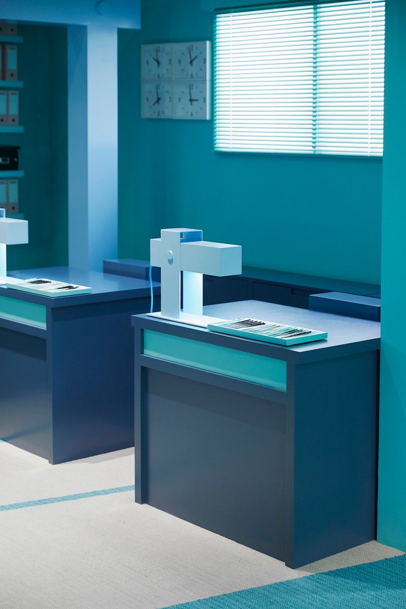 Exhibition space with stepped display platforms and white architectural model under venetian blinds