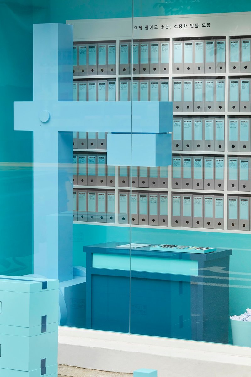 Glass partition reflecting rows of white binders on wall-mounted shelving with a low bench