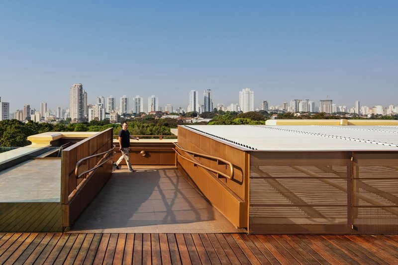 Rooftop terrace with timber louvers, decking, and a person walking with city skyline beyond