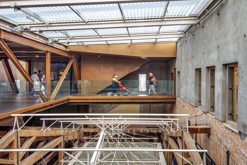 Multi-level atrium with exposed structural steelwork, glass balustrades, and concrete walls under translucent roof