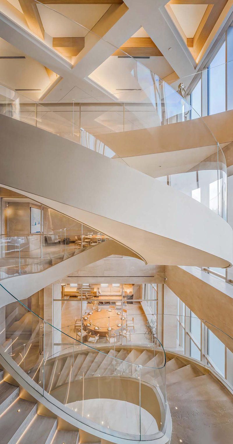 Atrium view of overlapping white ribbon stairs below geometric coffered ceiling with triangular panels