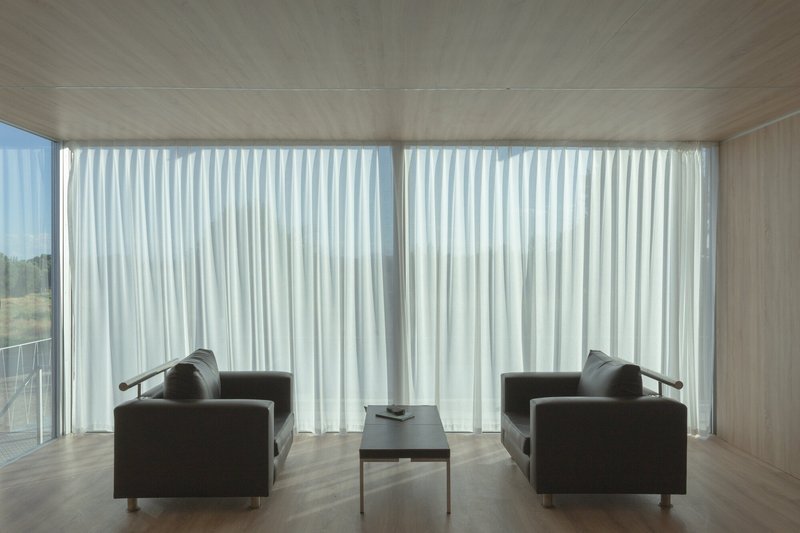 Interior living space with plywood ceiling and floor-to-ceiling white curtains filtering daylight