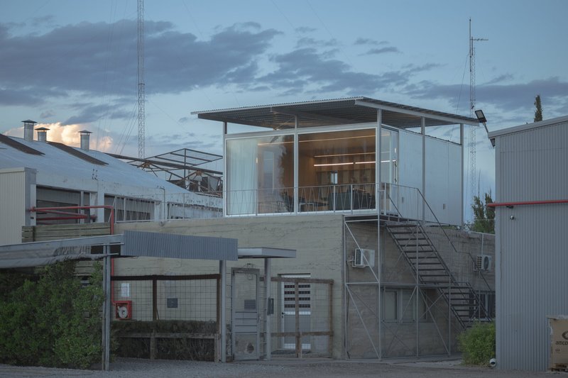 Glass box pavilion on concrete plinth accessed by external metal staircase under cloudy evening sky