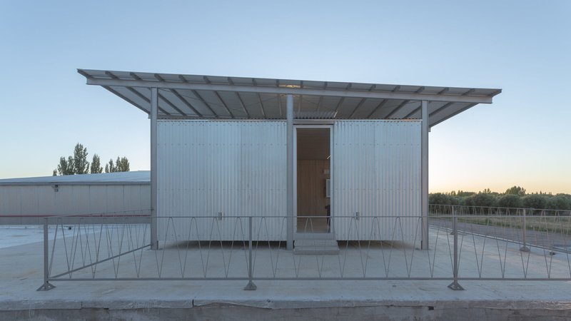 Front elevation of corrugated metal pavilion on a raised platform with exposed steel roof structure at sunset