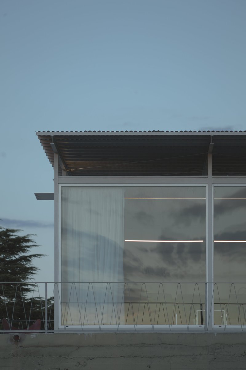 Corner detail of translucent polycarbonate wall with metal railing under corrugated roof overhang at twilight