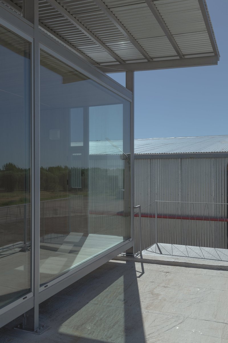 Glass-walled terrace with slatted metal canopy and corrugated metal screening wall on a concrete deck